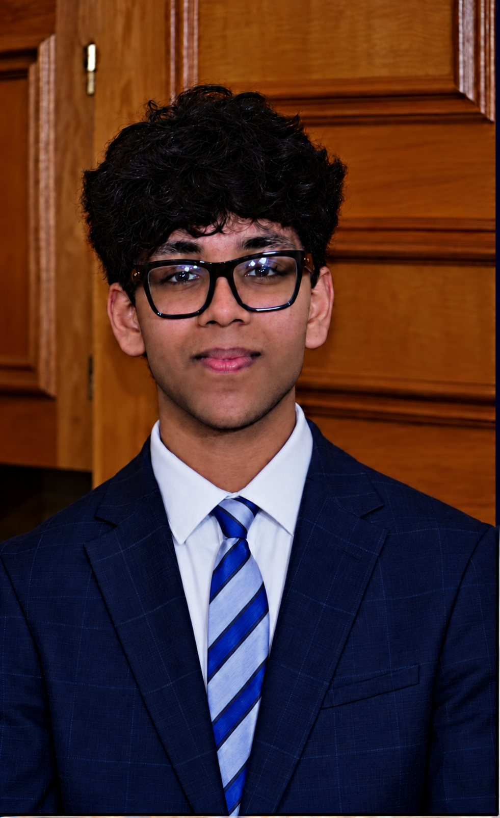 Nakshatr Velagapudi wearing glasses, a navy suit and a striped tie